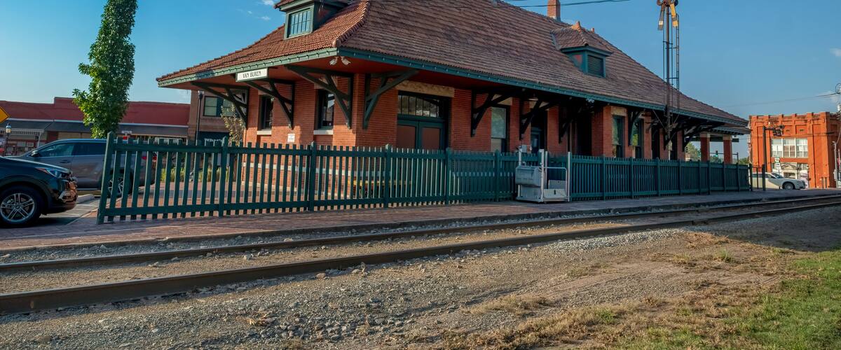 A vintage train station with a red roof, green fence, and a clear blue sky.