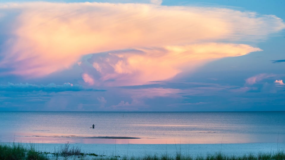 A sunset over a calm sea with a person standing on a small island.