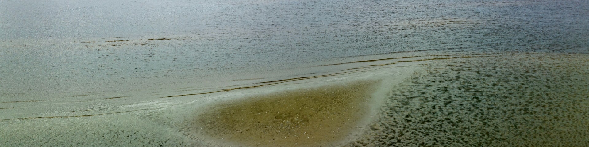 A vast body of water with a sandy beach and a cloudy sky.
