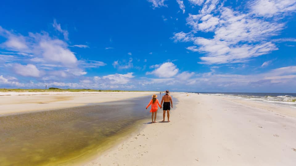 A beach with a clear sky and a couple walking along the shore.