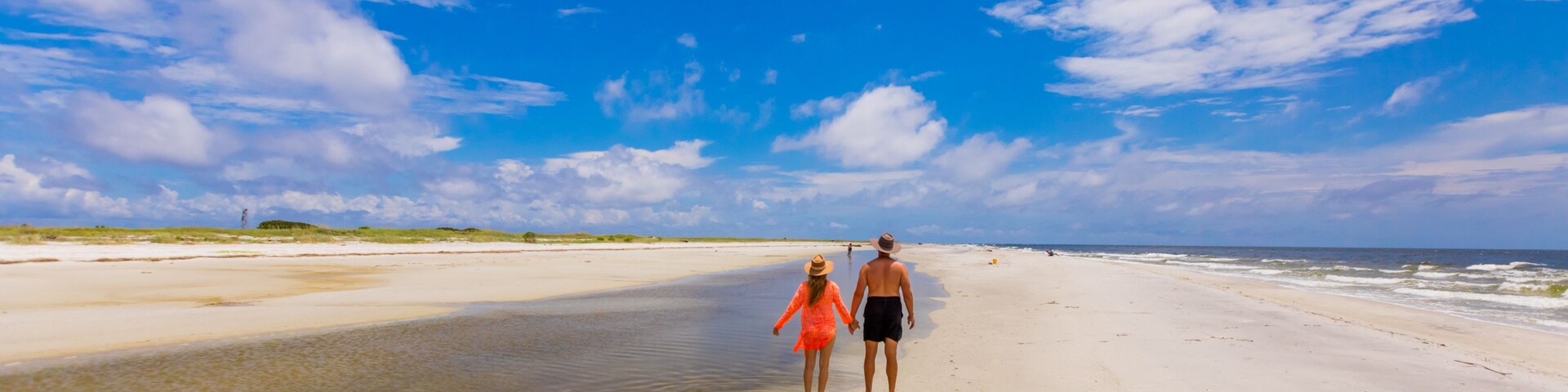 Uma praia com céu claro e um casal caminhando pela orla.