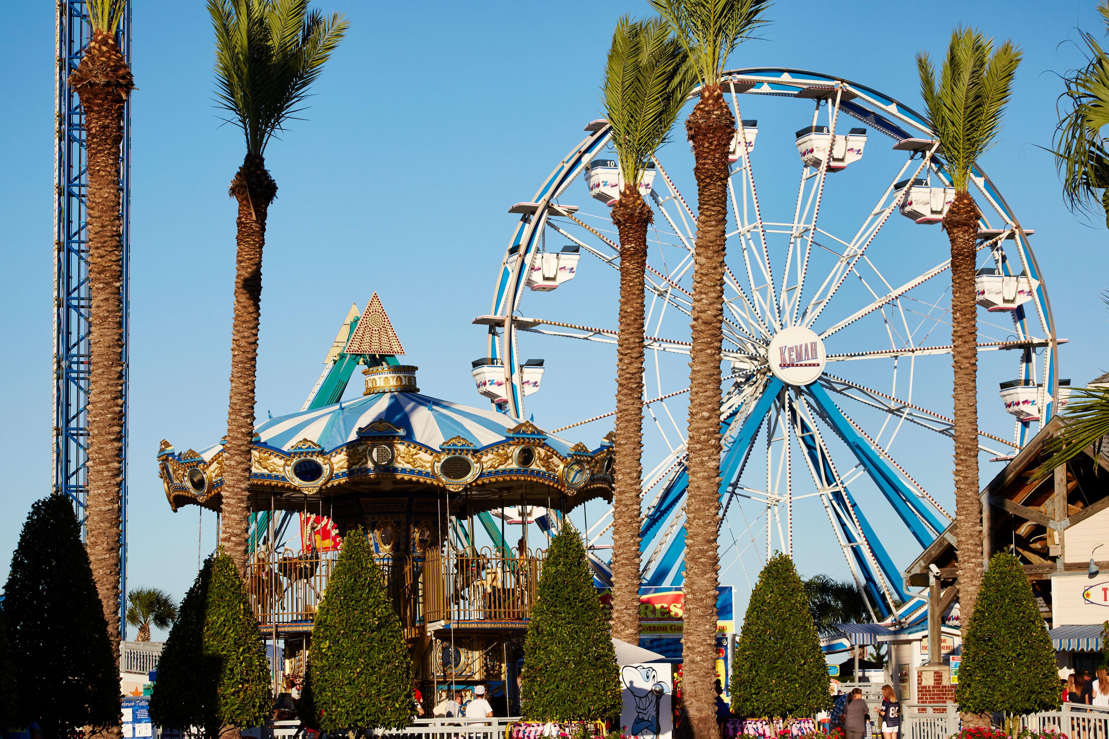 A Ferris wheel, a carousel, and palm trees at a fairground.