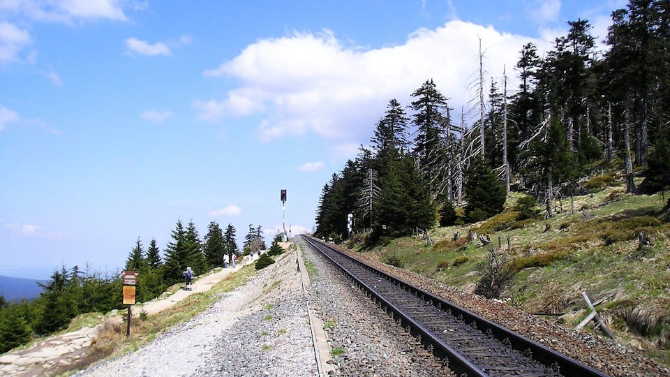 A railway track with a signal post and trees on a hillside.