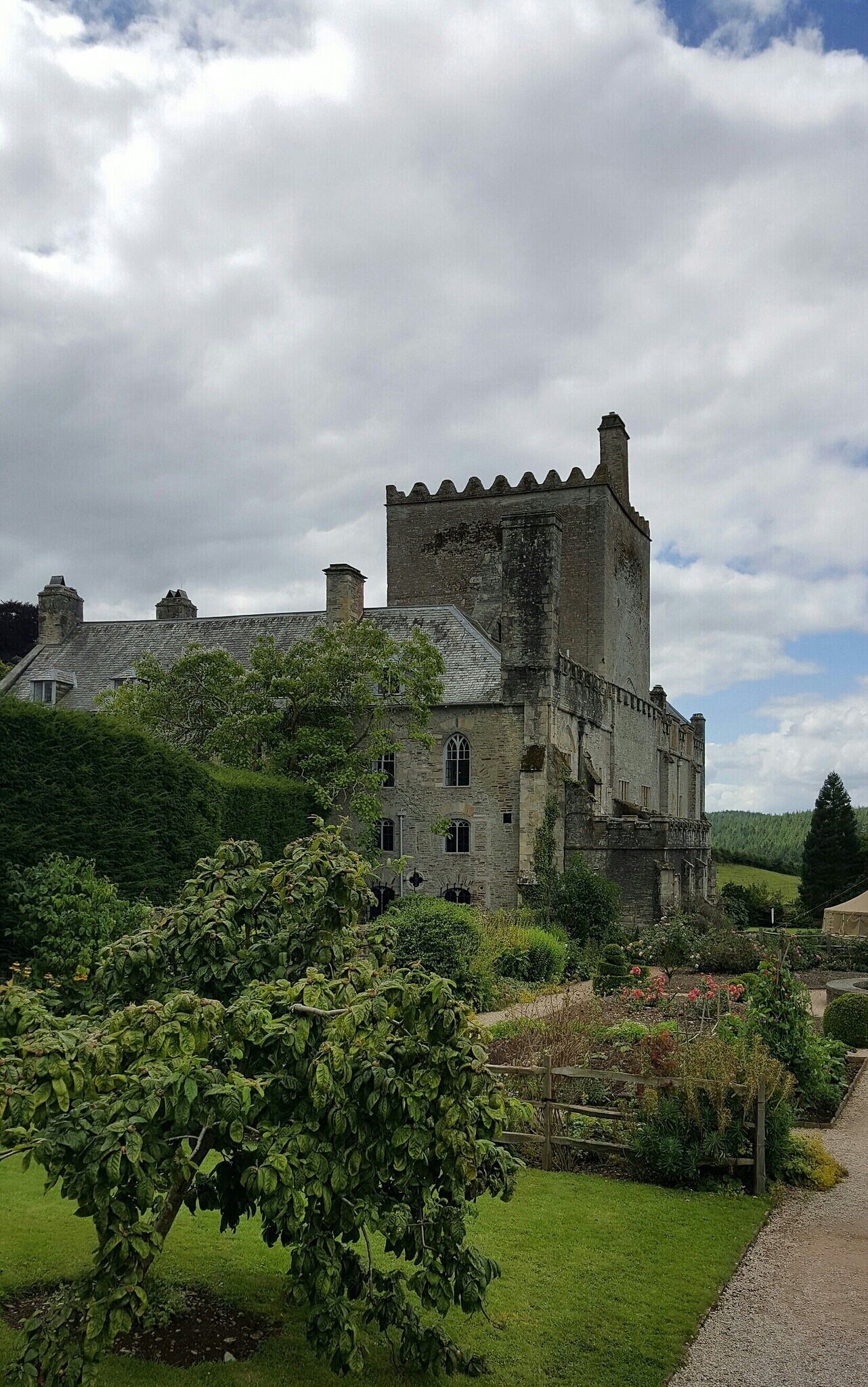 A historic stone castle with battlements, surrounded by lush greenery and a gravel path.