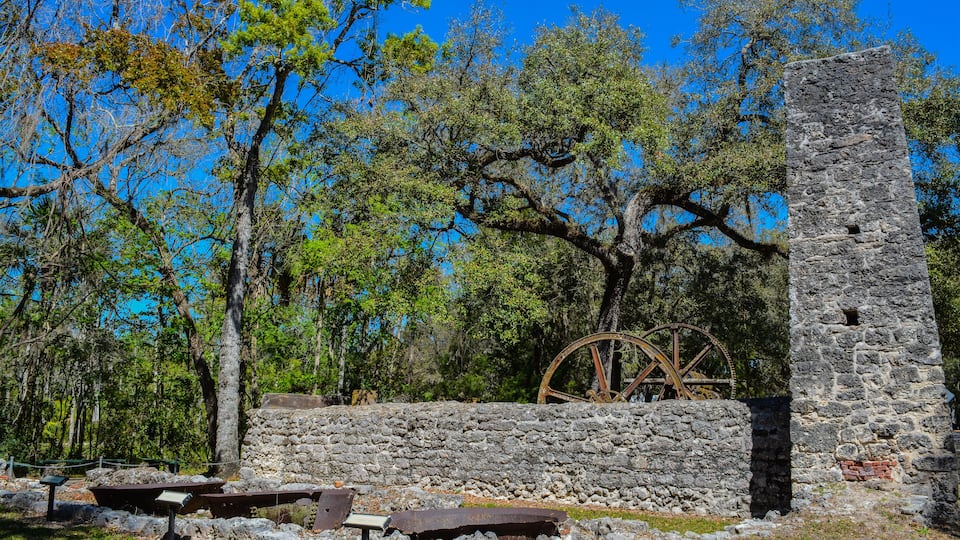 A historic stone tower and a large wooden water wheel in a forested area.