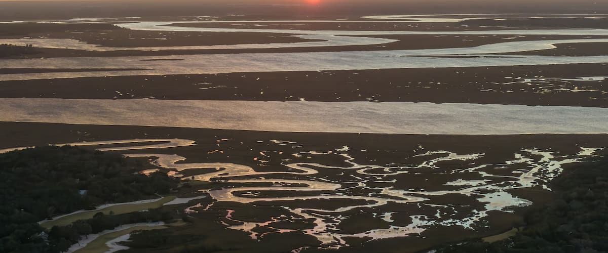 A sunset over a coastal landscape with water channels and sand dunes.