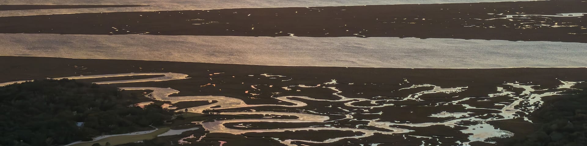 A sunset over a coastal landscape with water channels and sand dunes.
