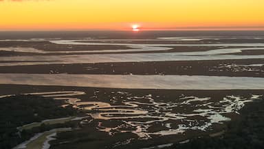 Um pôr do sol sobre uma paisagem costeira com canais de água e dunas de areia.