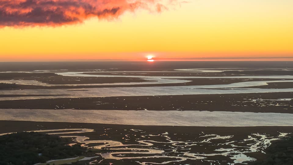 A sunset over a coastal landscape with water channels and sand dunes.