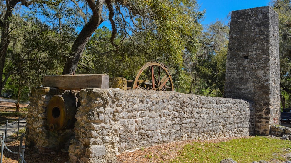 A historical water wheel and stone ruins in a wooded area.