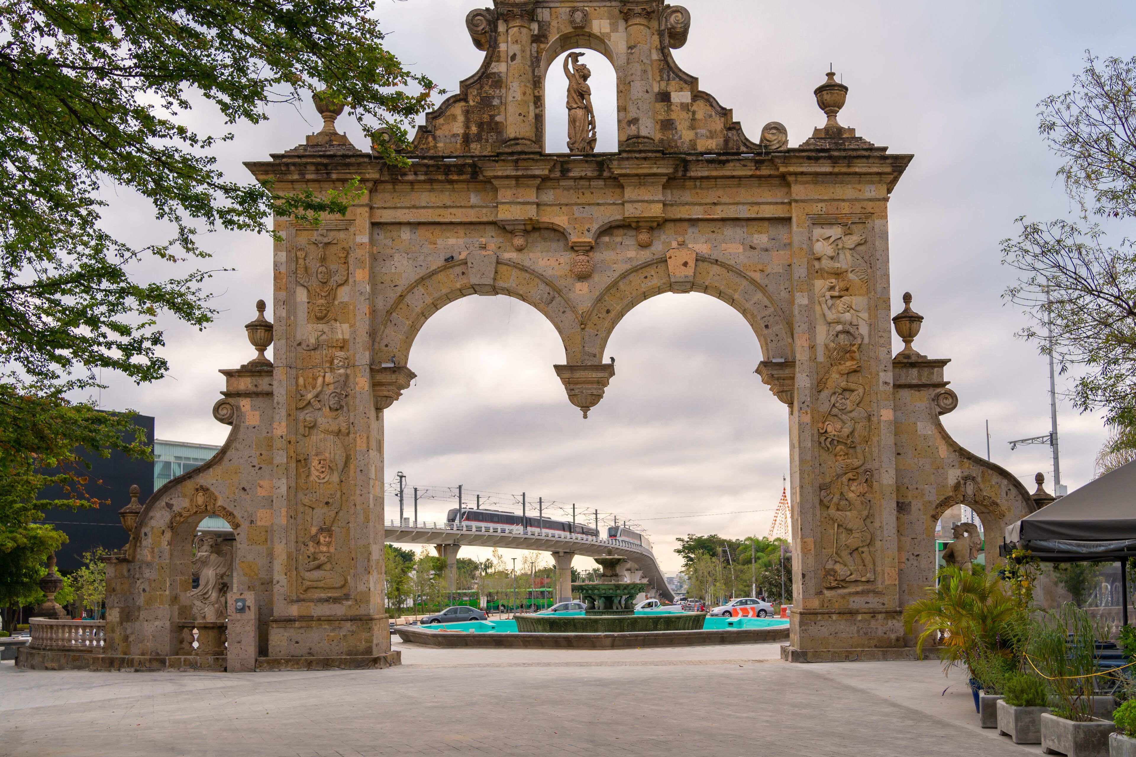 Un arco de piedra histórico con intrincados adornos y una fuente al frente.