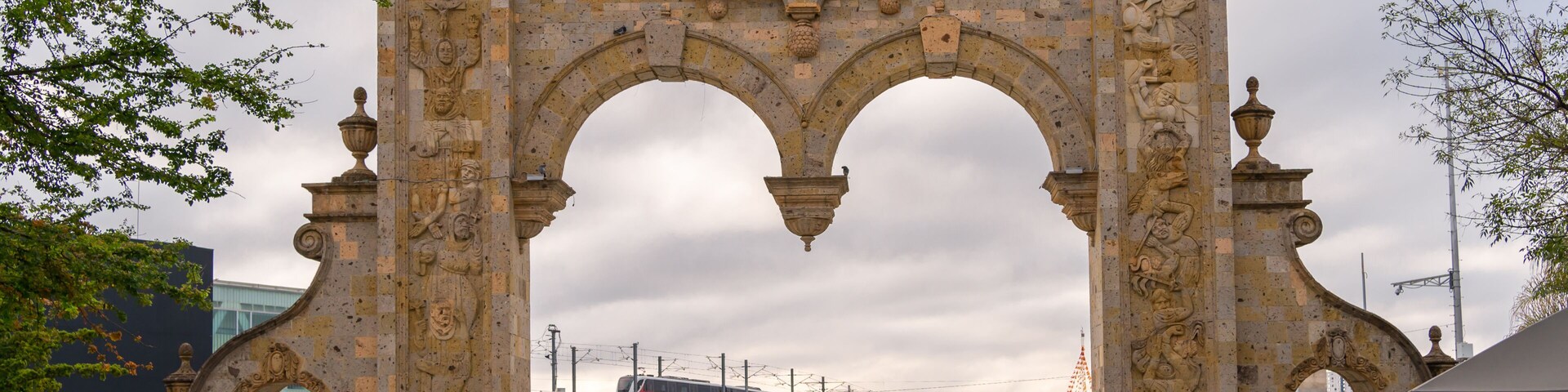 Un arco de piedra histórico con intrincados adornos y una fuente al frente.