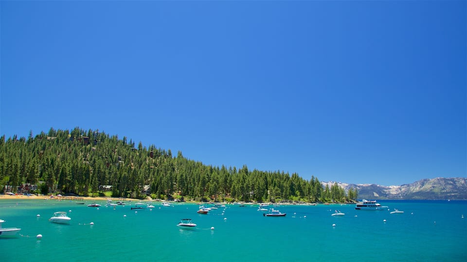 A turquoise sea with boats, a beach, and a forested hill.