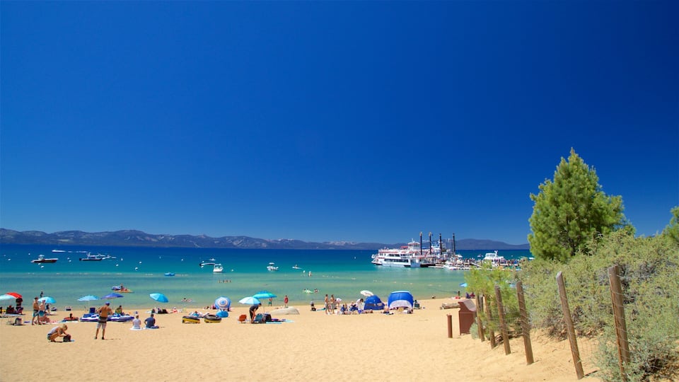 A beach with clear turquoise water, boats, and a distant mountain range.
