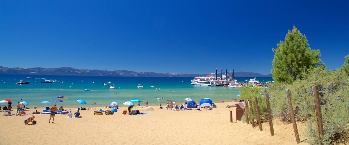 A beach with clear turquoise water, boats, and a distant mountain range.