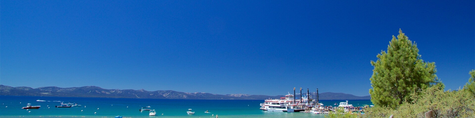 A beach with clear turquoise water, boats, and a distant mountain range.