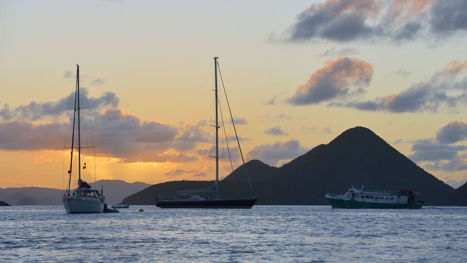 A sunset over a body of water with sailboats and a ferry.