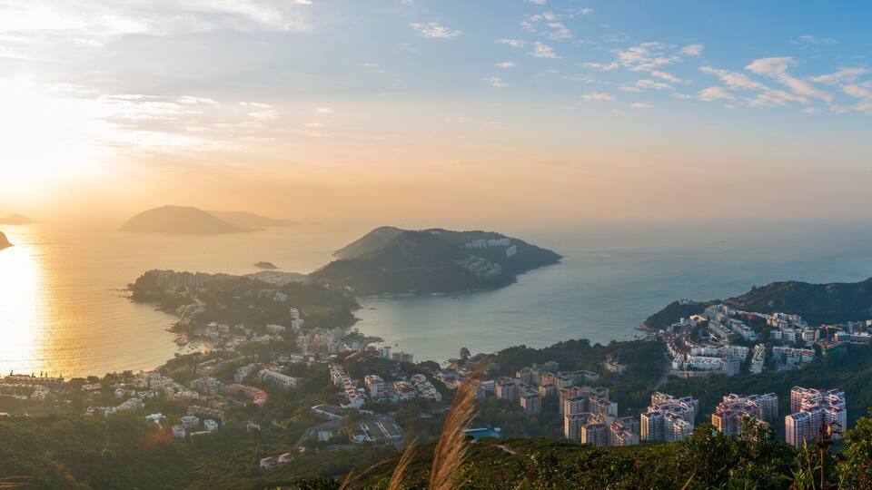 A coastal cityscape with mountains and a sunset over the sea.