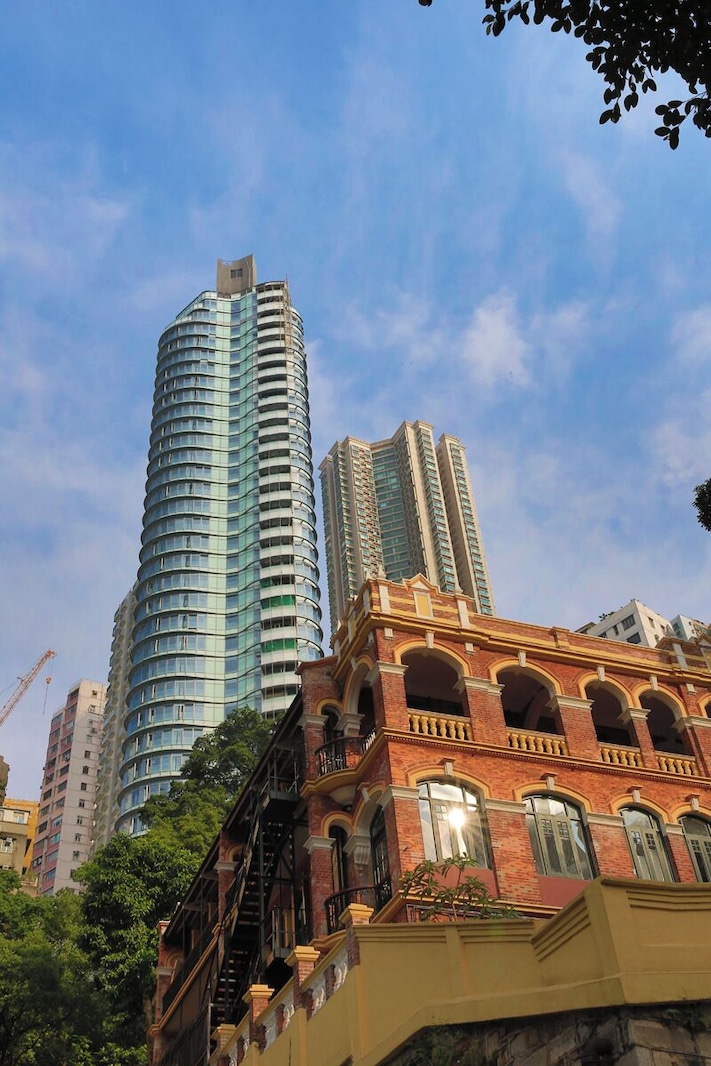A modern skyscraper with a curved facade, a historic red brick building with arched windows, and a clear blue sky.