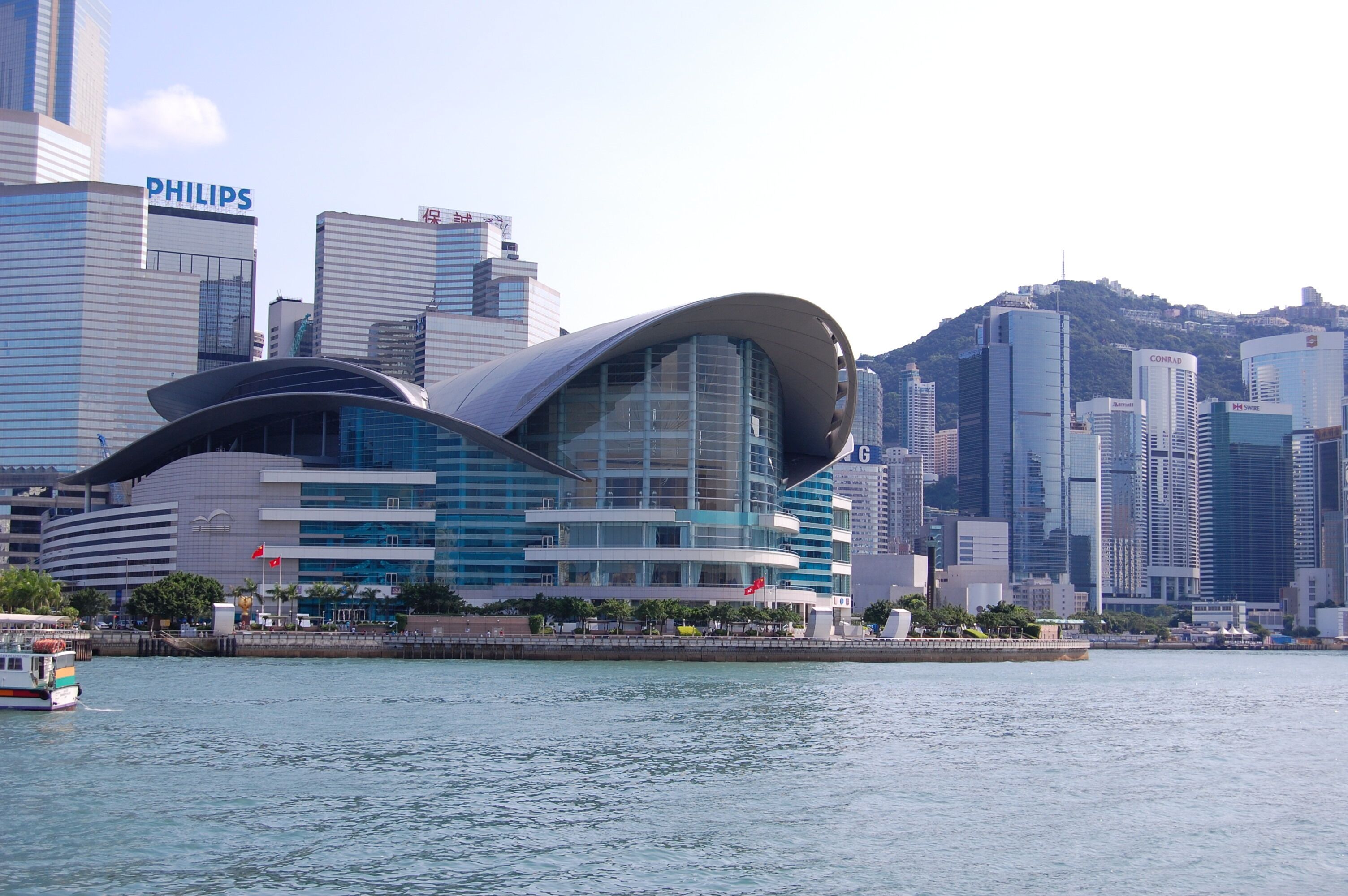 A modern building with a curved glass facade, surrounded by high-rise buildings and a body of water.