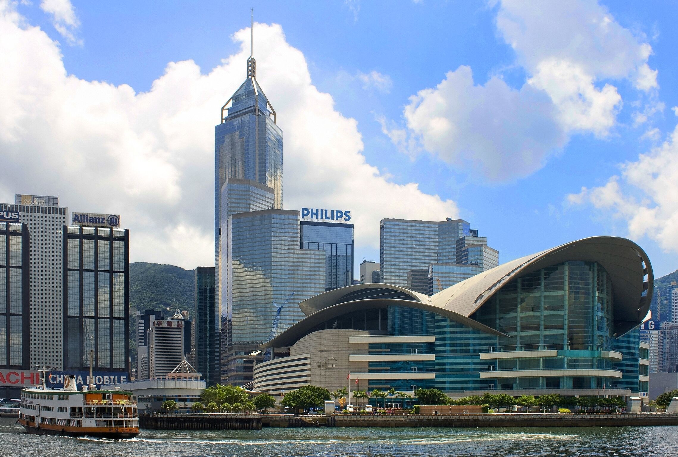 A modern cityscape with prominent buildings including a tall skyscraper with a pointed top and a curved building with a blue facade.