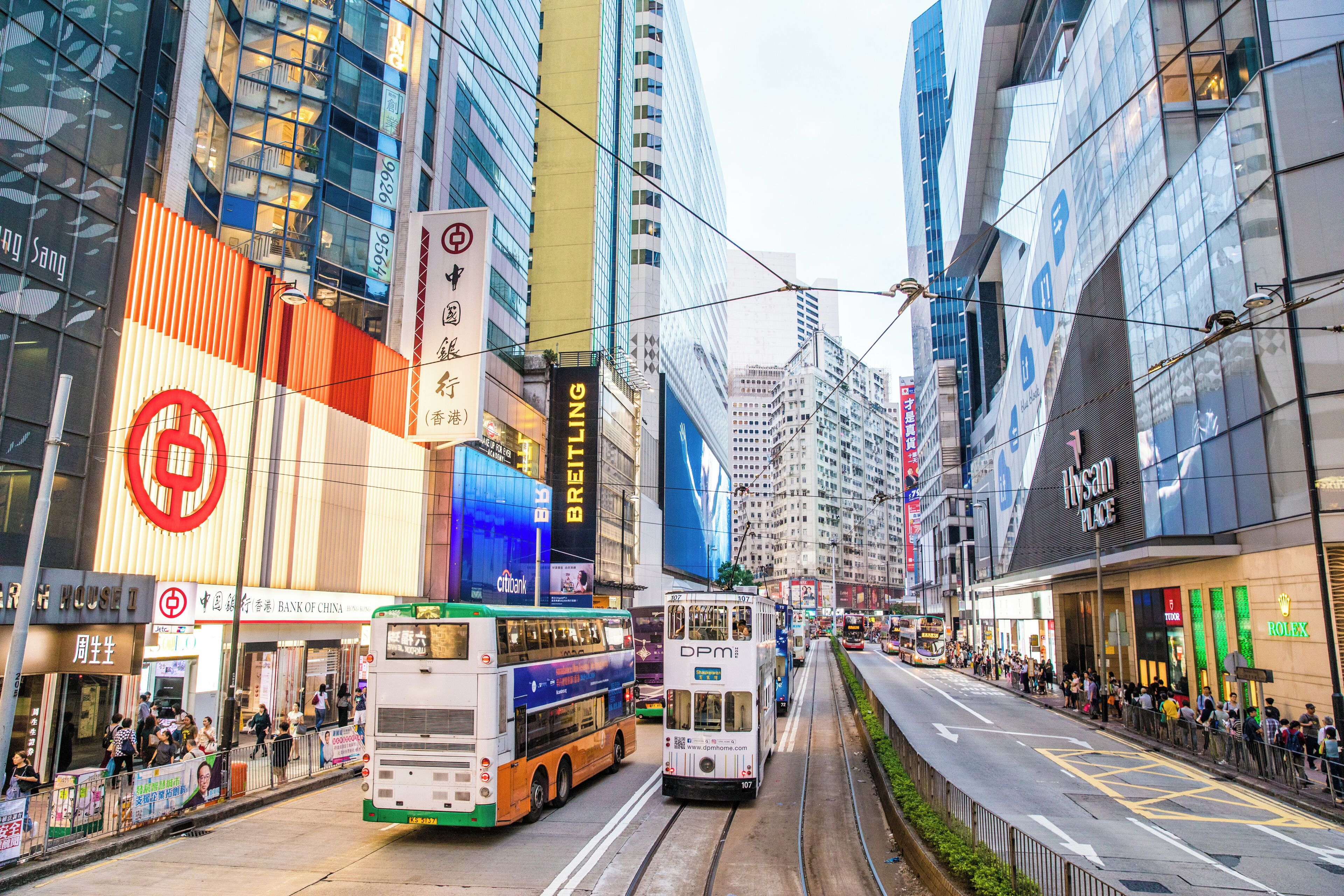 A busy urban street with modern buildings, a tram, and a bus.