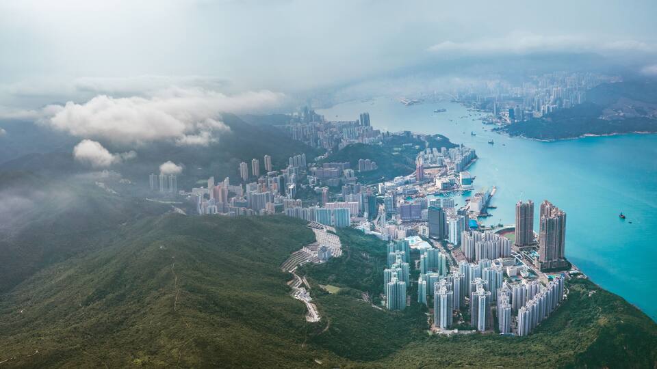 A coastal cityscape with high-rise buildings, a winding road, and a mountainous backdrop.