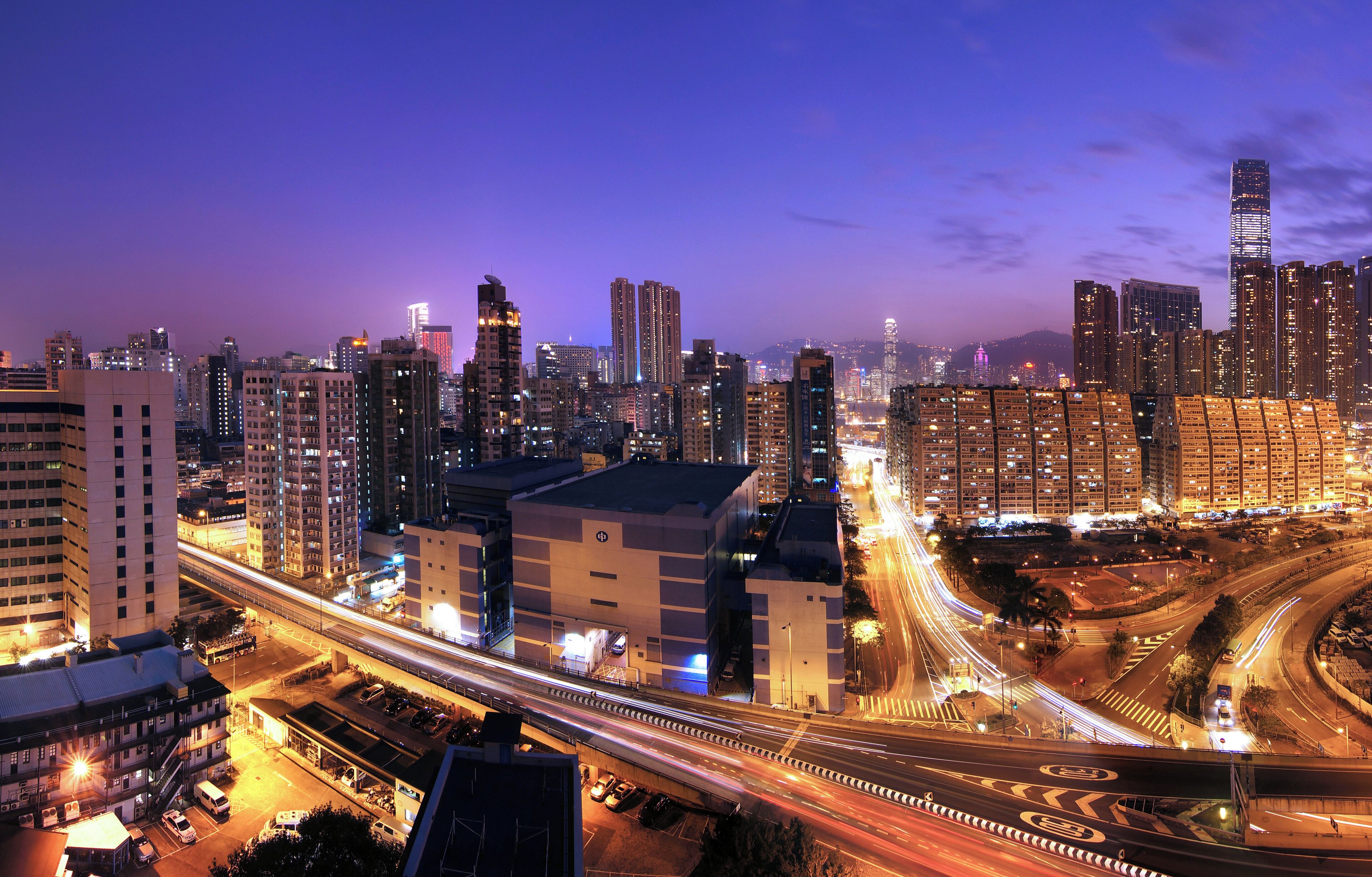 A cityscape at dusk with illuminated buildings and a multi-level highway.