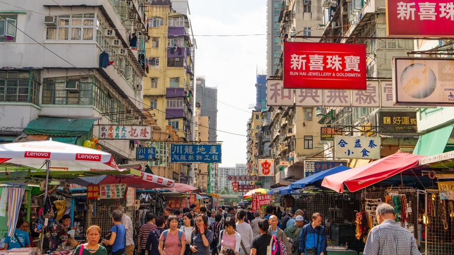 A bustling street market with various shops and stalls, surrounded by multi-story buildings.