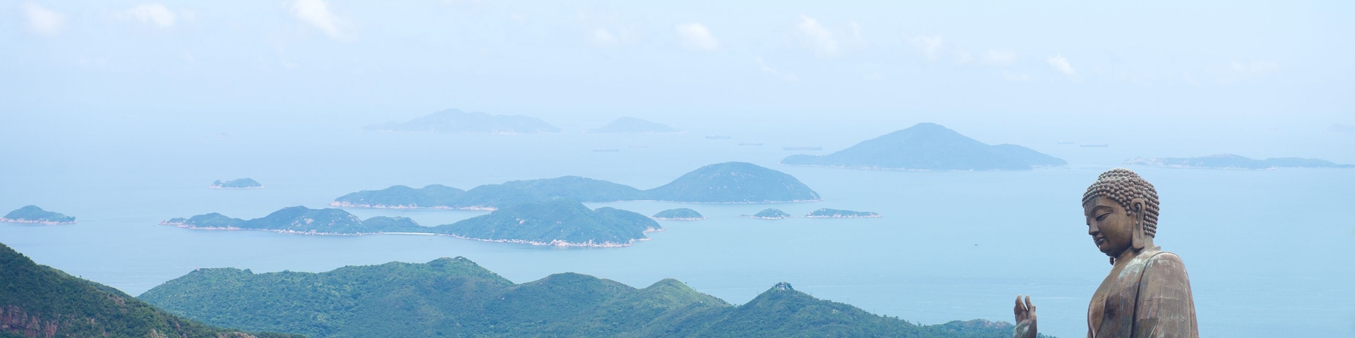 Uma grande estátua de Buda com vista para uma paisagem montanhosa, mar e ilhas.