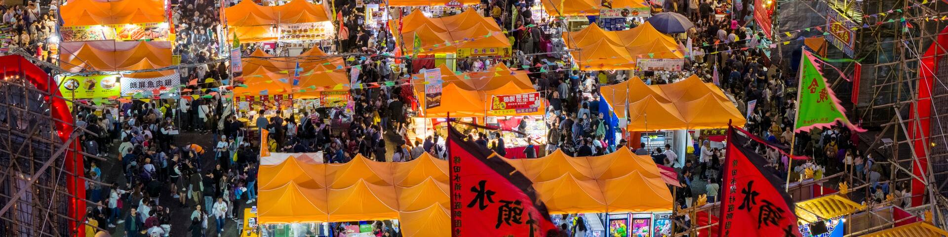 A crowded outdoor market with bright lights and orange tents.