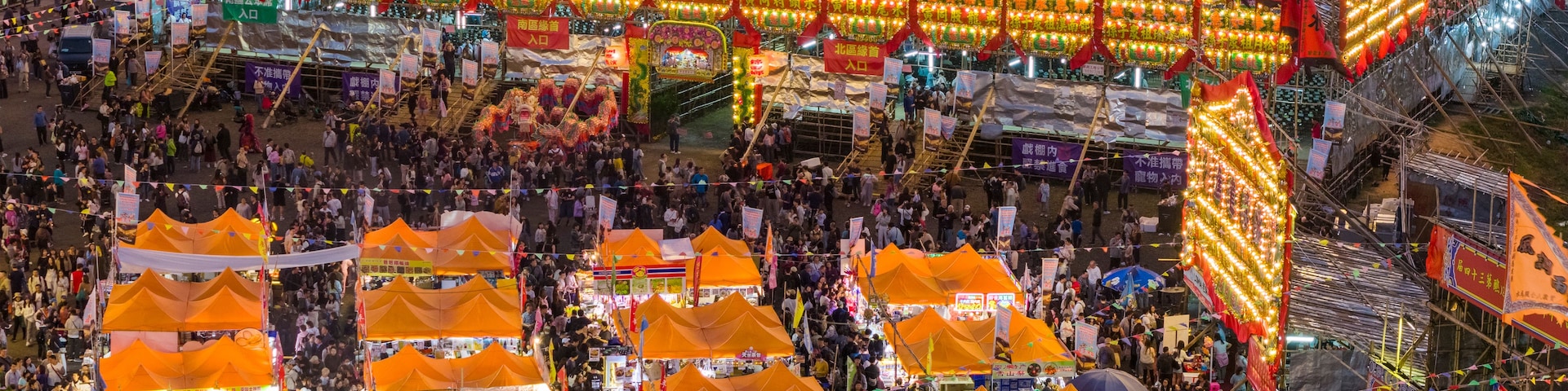 Un mercado al aire libre concurrido, con luces brillantes y carpas naranjas.
