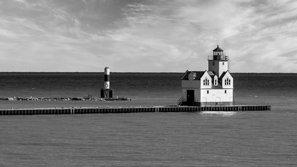 A lighthouse and a small building on a pier by the sea.