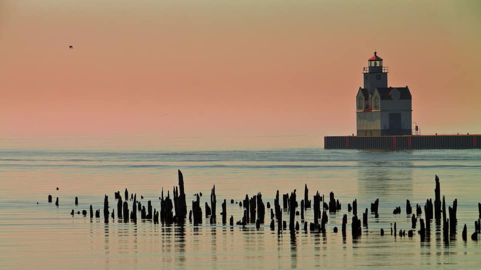 A lighthouse on a pier with a sunset sky.