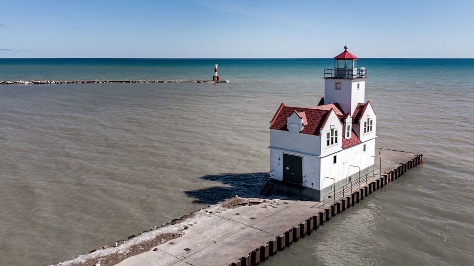 A white lighthouse with a red roof on a concrete pier extending into a calm body of water.