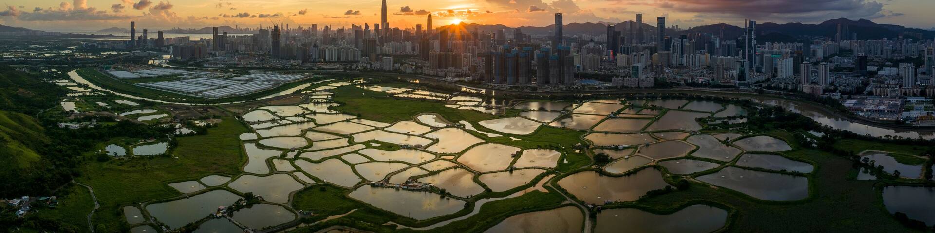 A cityscape with a river and terraced fields during sunset.