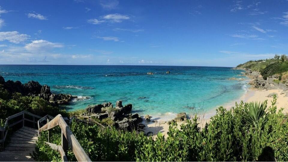 A coastal pathway leading to a beach with clear turquoise waters and lush greenery.