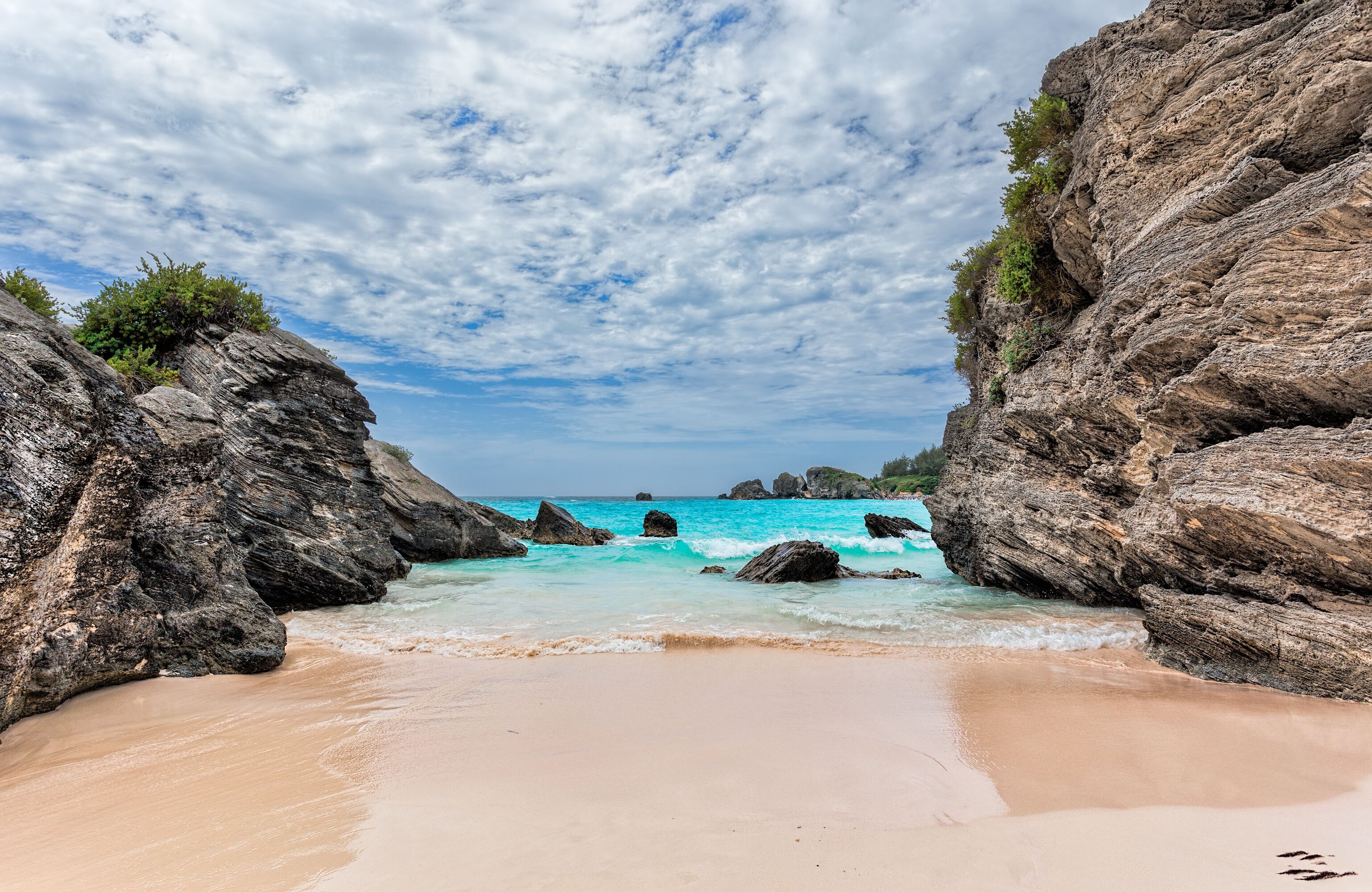 A beach with clear turquoise waters, rocky cliffs, and a sandy shore.