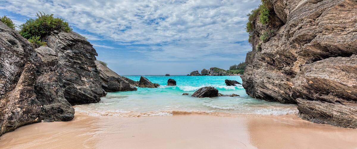 A beach with clear turquoise waters, rocky cliffs, and a sandy shore.
