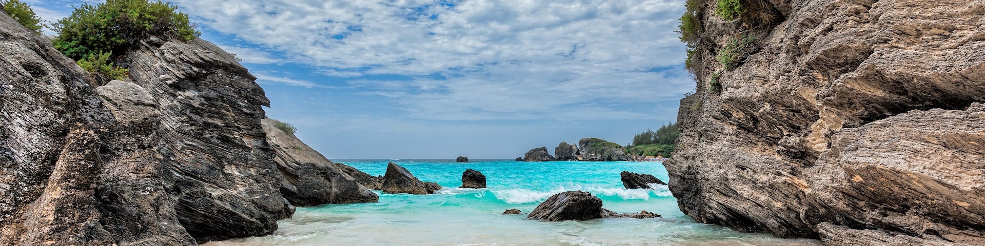 A beach with clear turquoise waters, rocky cliffs, and a sandy shore.
