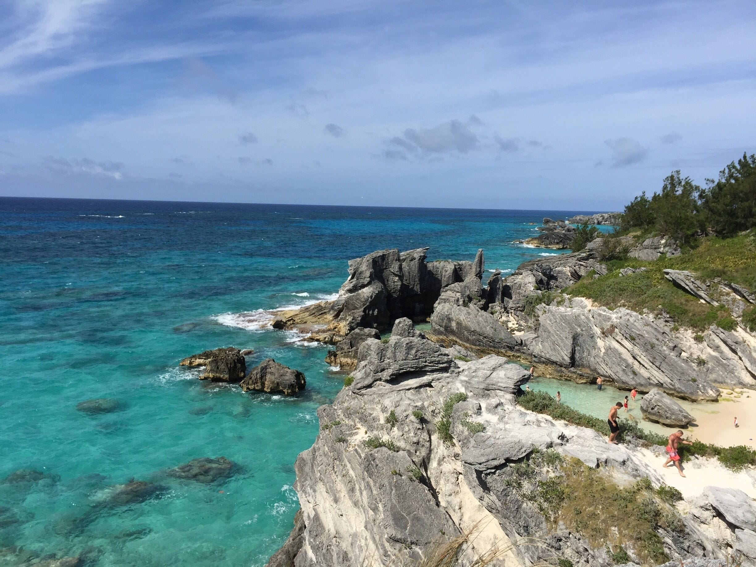 A rocky coastline with clear turquoise waters and a sandy beach.
