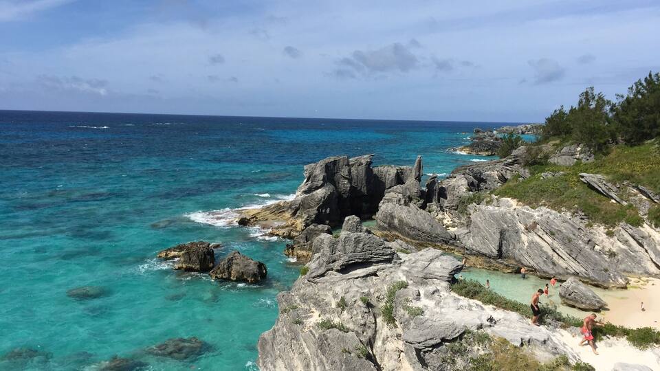 A rocky coastline with clear turquoise waters and a sandy beach.