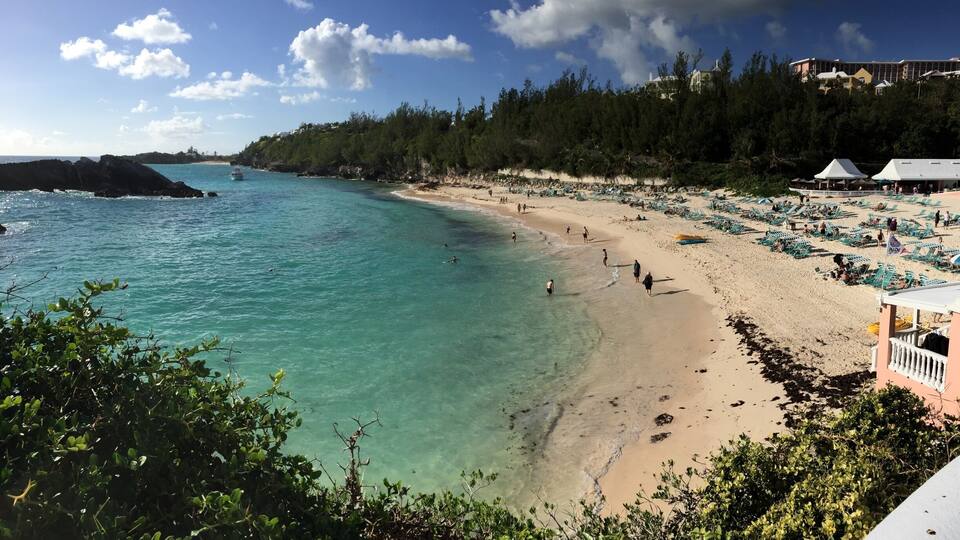 A beach with clear turquoise waters, sandy shore, and lush greenery.