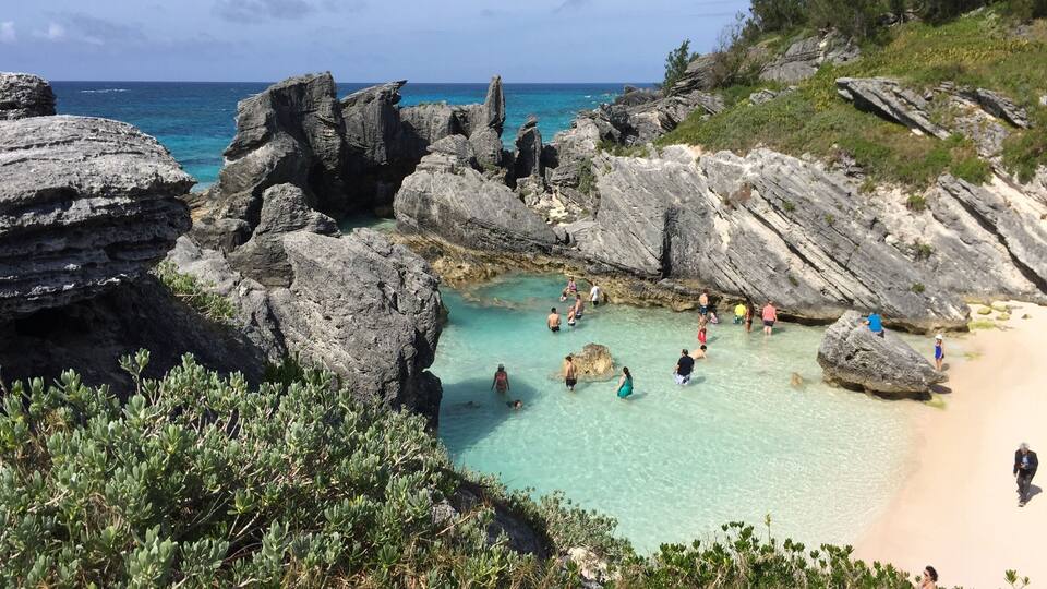 A rocky coastline with clear turquoise waters, a sandy beach, and lush greenery.