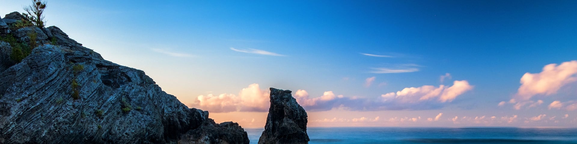 A coastal landscape with a prominent rock formation in the sea, a sandy beach, and a clear sky.