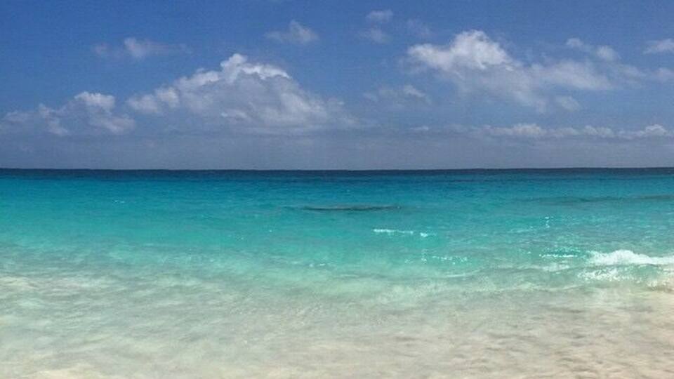 A beach with clear turquoise water and a sandy shore under a blue sky with scattered clouds.
