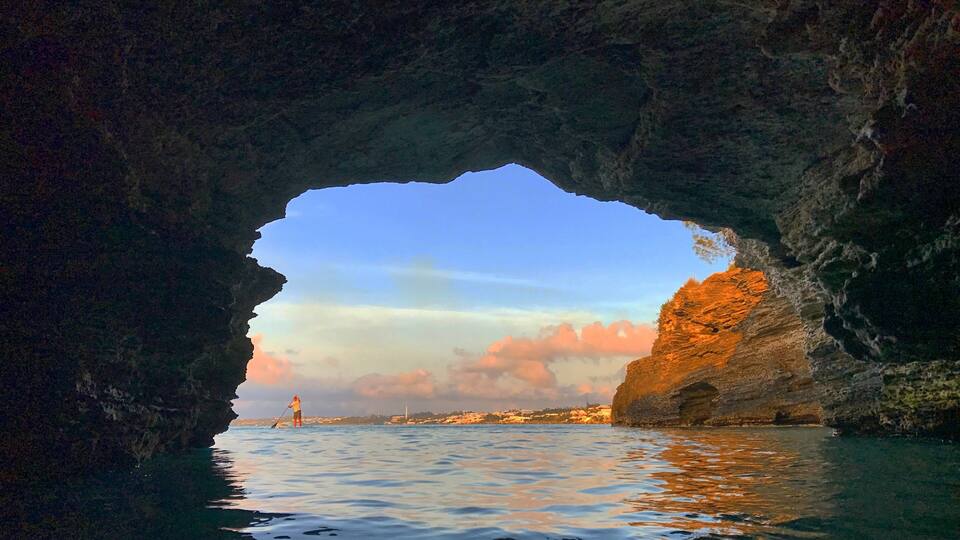 A cave opening to a coastal scene with calm water and a sunset sky.