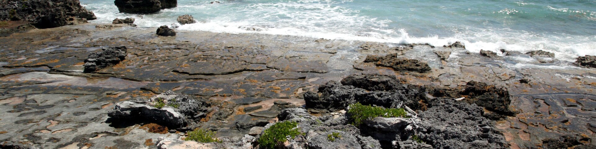 A rocky shoreline with waves crashing against the rocks and the ocean in the background.