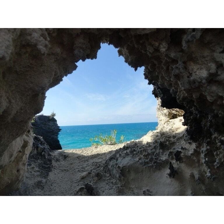 A cave opening to a beach with clear blue water and a sandy shore.