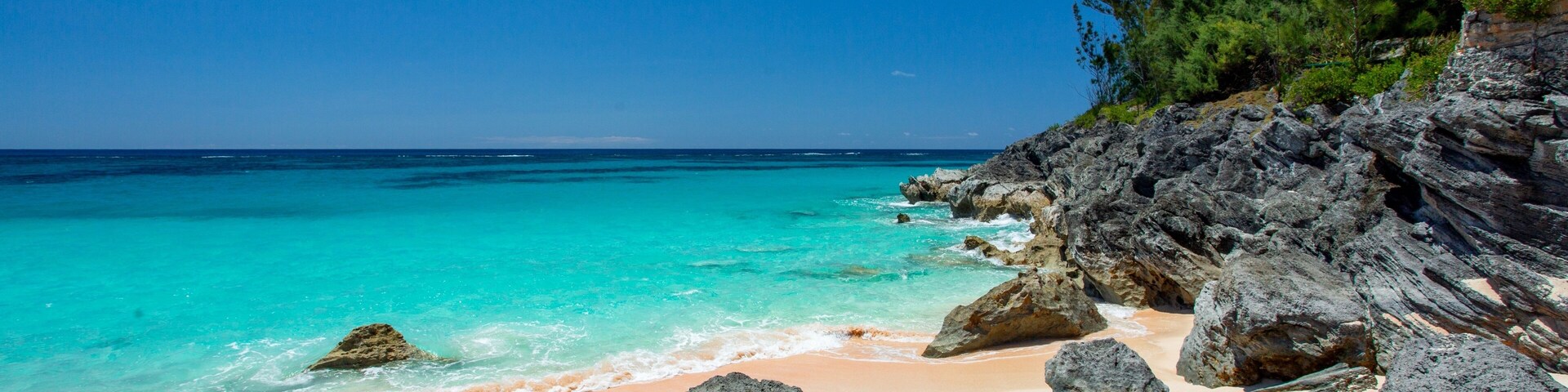 Una playa con aguas turquesas cristalinas, arena dorada y afloramientos rocosos.